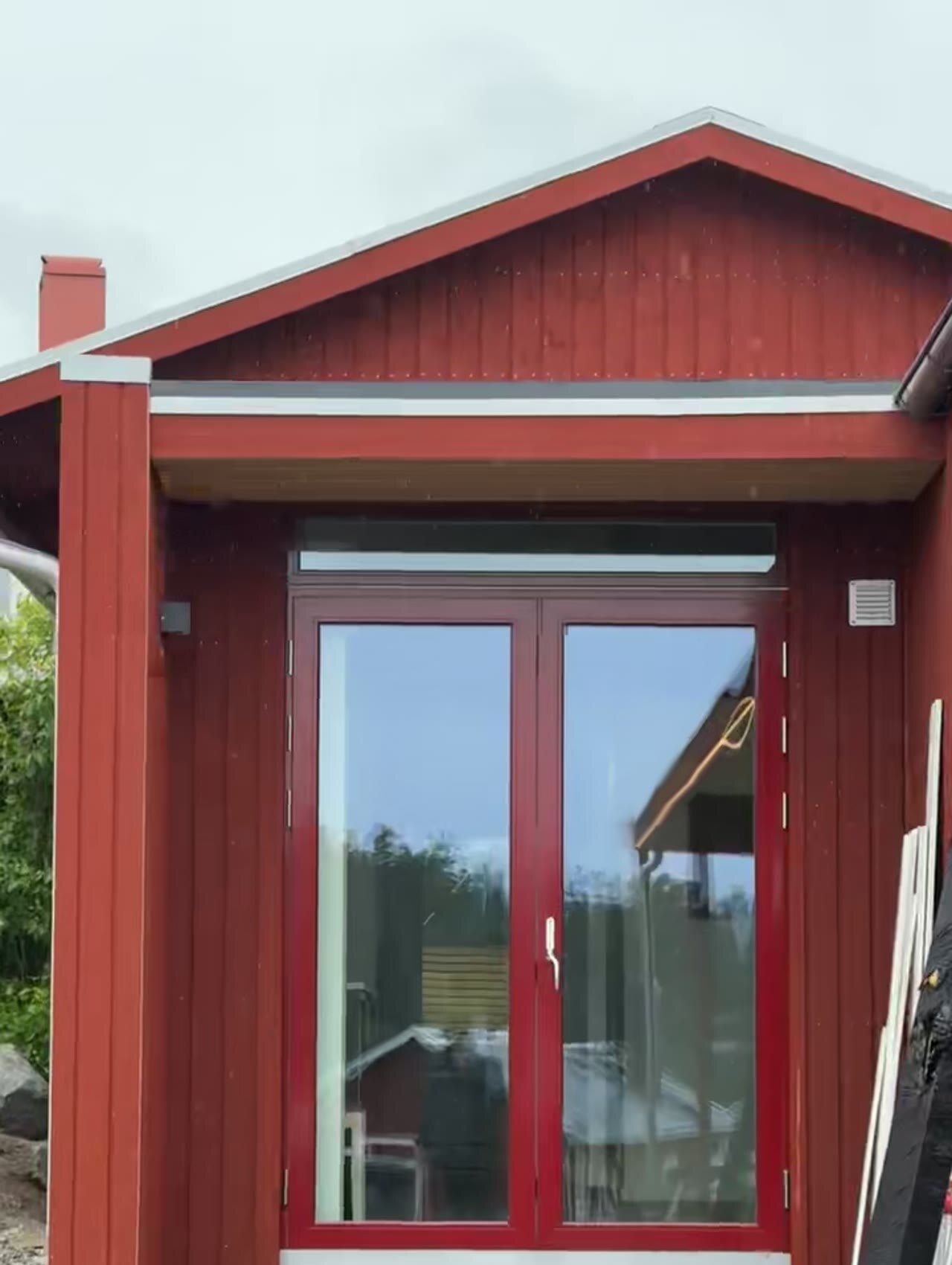 Rödmålat hus med nyrenoverade dubbla glasdörrar och träpanel under övertak