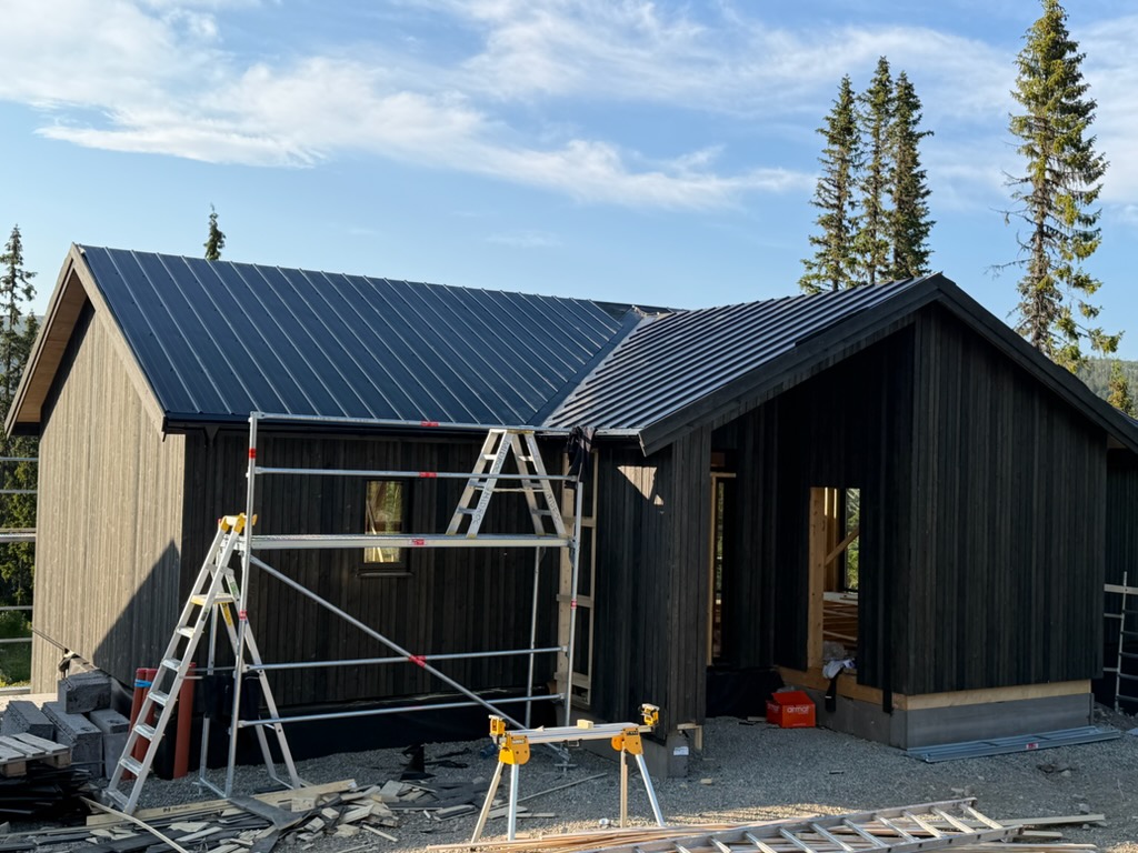 Hus med svart träpanel och plåttak under byggnation